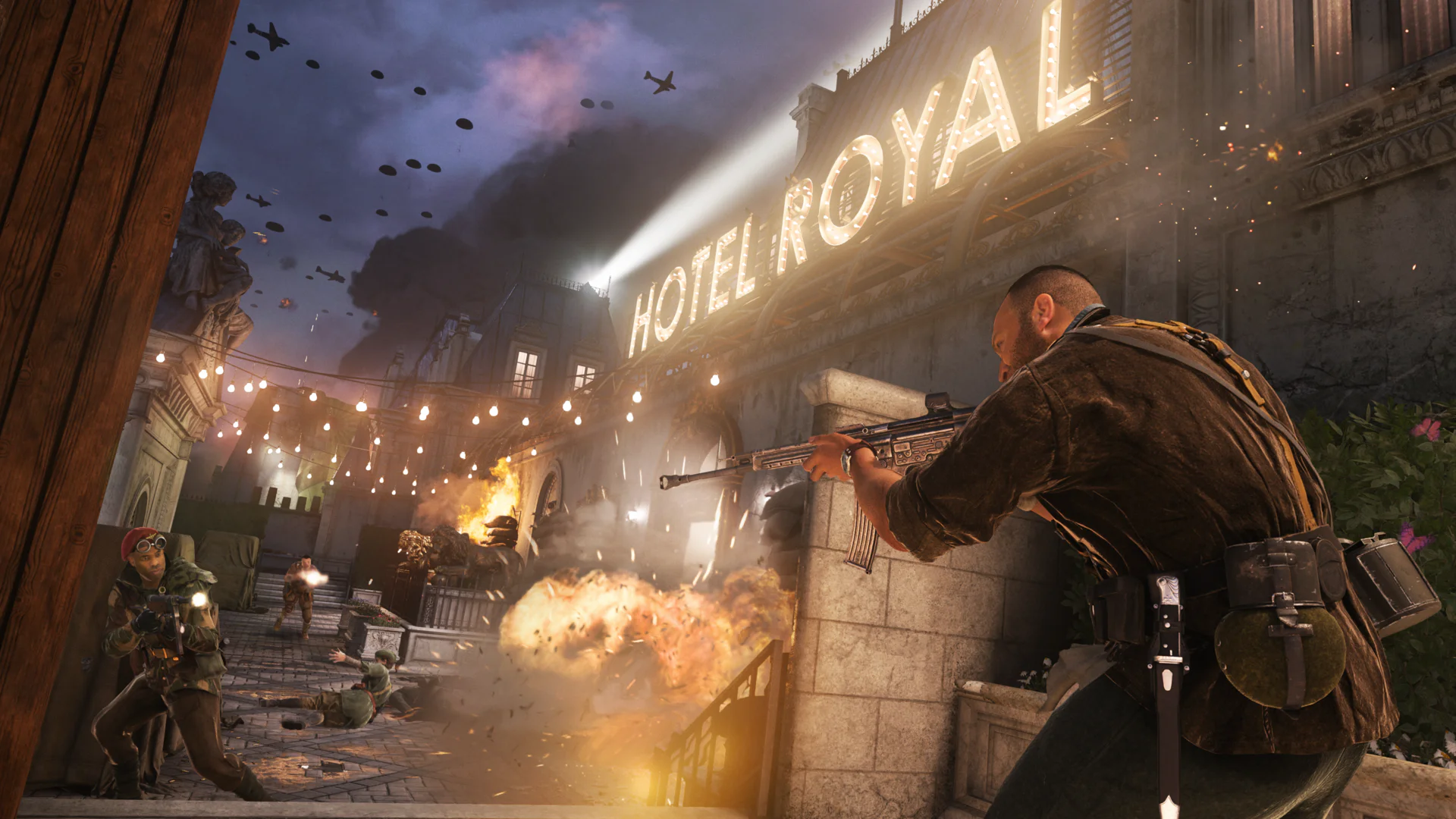 Сцена боя в игре Call of Duty Vanguard, солдаты сражаются у отеля, на заднем плане горит танк и летят самолеты.